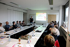 Personen sitzen an großem Tisch bei einem Abend-Seminar.