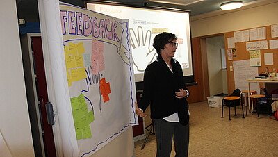 Person steht neben einer Tafel und trägt etwas vor