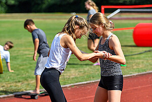 zwei Mädchen unterstützen sich gegenseitig im Schulsport
