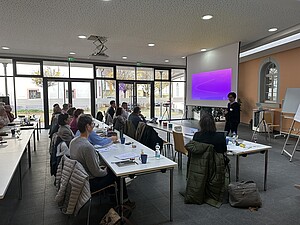 Personen sitzen an Tischen und hören Referenten zu