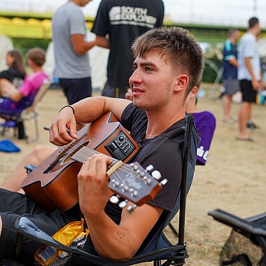 Symbolbild Teilnehmer spielt Gitarre auf dem Zeltplatz im Camp Breisach 2026