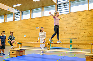 Mädchen balanciert vor Lehrerin auf Balken.