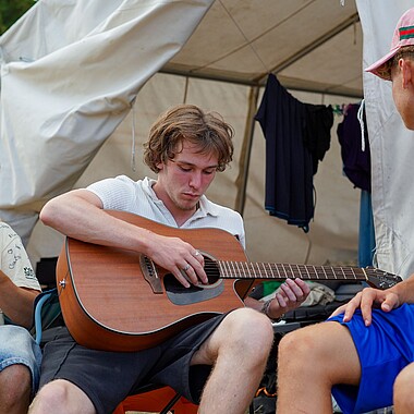 Symbolbild Teilnehmer spielt Gitarre auf dem Zeltplatz im Camp Breisach 2026