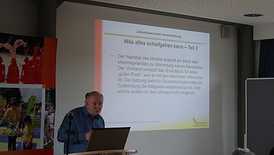 Person hält neben einer Leinwand einen Vortrag