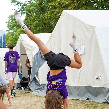 Symbolbild Teilnehmerin macht einen Handstand auf dem Zeltplatz im Camp Breisach 2026
